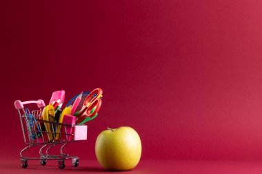 Okul malzemeleri, elma ve fotokopi alanının olduğu minyatür alışveriş arabasının önünü kapatın. Okula dönüş, alışveriş, okul malzemeleri, öğrenme, okul ve eğitim kavramı.