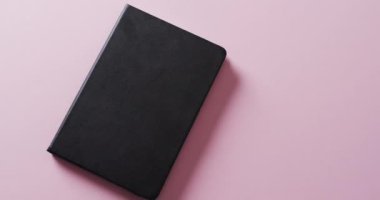 Pembe arka planda fotokopi alanı olan kapalı siyah kitabı yavaş çekimde kapat. Edebiyat, okuma ve kitaplar.