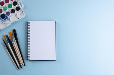 Boyaları, defterleri ve mavi arkaplanda fotokopi alanı olan fırçaları kapat. Okula dönüş, sanat, resim, okul malzemeleri, öğrenme, okul ve eğitim kavramı.