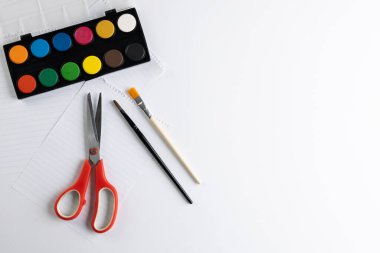 Beyaz arkaplanda fotokopi alanı olan boya, kağıt, makas ve fırçaları kapatın. Okula dönüş, sanat, resim, okul malzemeleri, öğrenme, okul ve eğitim kavramı.