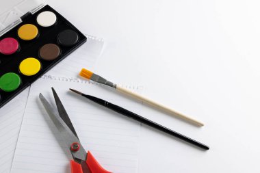 Beyaz arkaplanda fotokopi alanı olan boya, kağıt, makas ve fırçaları kapatın. Okula dönüş, sanat, resim, okul malzemeleri, öğrenme, okul ve eğitim kavramı.
