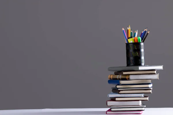 Stack of books and notebooks with pencil container on top and copy space on grey background. Reading, learning, school and education concept.