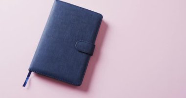 Kapalı mavi defterin üzerinde pembe arkaplan olan kopyasını yavaş çekimde kapat. Edebiyat, okuma ve kitaplar.