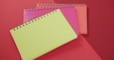 Kırmızı arkaplandaki renkli defterlerin genel görünümü, yavaş çekimde. Kırtasiye, öğrenim, okul ve eğitim kavramı.