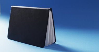 Açık siyah kitabın mavi arkaplandaki fotokopi alanını yavaş çekimde yatay olarak kapat. Edebiyat, okuma ve kitaplar.