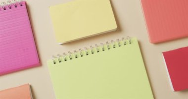 Bej arkaplan üzerine dizilmiş renkli defterlerin genel görünümü yavaş çekimde. Kırtasiye, öğrenim, okul ve eğitim kavramı.
