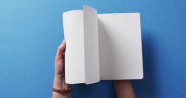 Yavaş çekimde, mavi arkaplanda kopya alanı olan el yapraklarını kitabın içinde kapat. Edebiyat, okuma, boş zaman ve kitaplar..