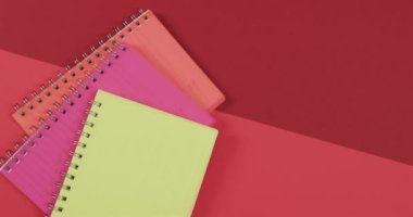 Kırmızı arkaplanda fotokopi alanı olan renkli defterlerin genel görünümü yavaş çekimde. Kırtasiye, öğrenim, okul ve eğitim kavramı.