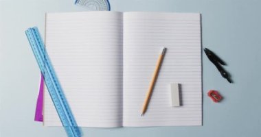 Mavi arka planda okul kırtasiyesi olan açık defterin genel görünümü, yavaş çekimde. Kırtasiye, öğrenim, okul ve eğitim kavramı.