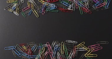 Siyah arka planda fotokopi alanı olan dağınık renkli ataçların genel görünümü yavaş çekimde. Kırtasiye, öğrenim, okul ve eğitim kavramı.