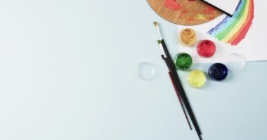 Not defterinin yukarıdan görünüşü, mavi arka planda fırçalar ve boyalar fotokopi alanı ile, yavaş çekimde. Kırtasiye, yaratıcılık, öğrenme, okul ve eğitim kavramı.