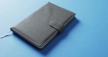 Kapalı gri defteri mavi arkaplanda yavaş çekimde kopyalama alanı ile kapat. Edebiyat, okuma ve kitaplar.