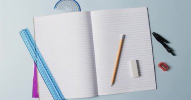 Mavi arka planda okul kırtasiyesi olan açık defterin genel görünümü, yavaş çekimde. Kırtasiye, öğrenim, okul ve eğitim kavramı.