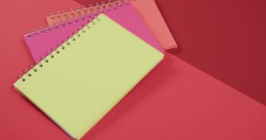 Kırmızı arkaplandaki renkli defterlerin genel görünümü, yavaş çekimde. Kırtasiye, öğrenim, okul ve eğitim kavramı.