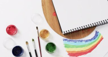 Not defterinin yukarıdan görünüşü, beyaz arka planda fırçalar ve boyalar fotokopi alanı ile, yavaş çekimde. Kırtasiye, yaratıcılık, öğrenme, okul ve eğitim kavramı.