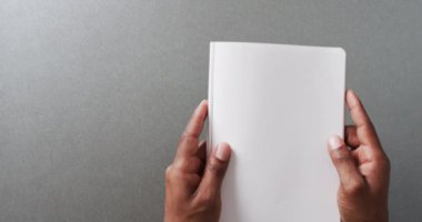 Gri arkaplan üzerine kopya alanı olan kitabı yavaş çekimde tutan elleri kapatın. Edebiyat, okuma, boş zaman ve kitap.