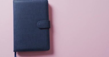 Kapalı mavi defterin üzerinde pembe arkaplan olan kopyasını yavaş çekimde kapat. Edebiyat, okuma ve kitaplar.