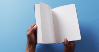 Yavaş çekimde, mavi arkaplanda kopya alanı olan kitapların arasında el kapaklarını kapatın. Edebiyat, okuma, boş zaman ve kitap.