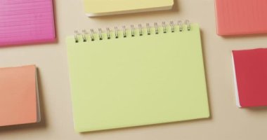 Bej arkaplan üzerine dizilmiş renkli defterlerin genel görünümü yavaş çekimde. Kırtasiye, öğrenim, okul ve eğitim kavramı.