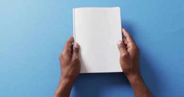 Yavaş çekimde, mavi arkaplanda kopya alanı olan el yapraklarını kitabın içinde kapat. Edebiyat, okuma, boş zaman ve kitaplar..