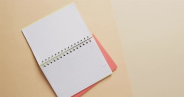 Bej arka planda pembe kalemli açık defter görüntüsü, yavaş çekimde. Kırtasiye, öğrenim, okul ve eğitim kavramı.
