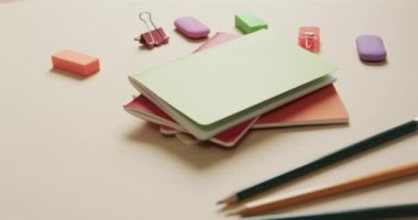 Bej arka planda okul kağıtları olan renkli defterleri yavaş çekimde kapat. Kırtasiye, öğrenim, okul ve eğitim kavramı.