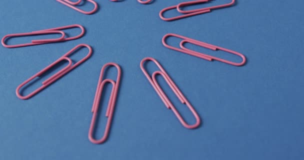 关闭粉红色的回形针设置在蓝色的背景上 慢动作 文具用品 学校和教育概念 — 图库视频影像
