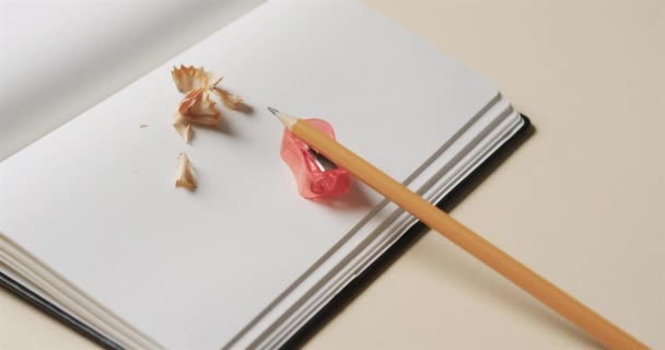 ベージュの背景に鉛筆と鉛筆のシャープナーで開いたノートブックの閉じる スローモーションで 文房具 教育の概念 — ストック動画