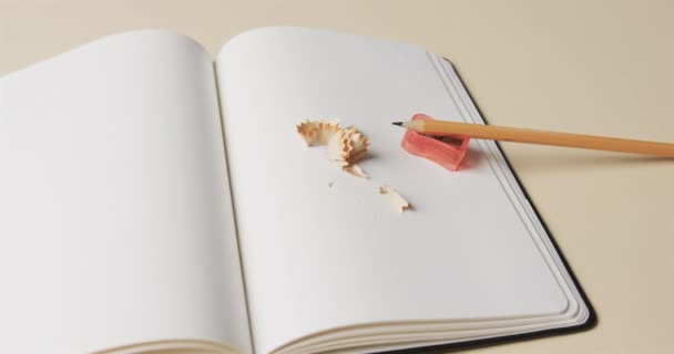 ベージュの背景に鉛筆と鉛筆のシャープナーで開いたノートブックの閉じる スローモーションで 文房具 教育の概念 — ストック動画