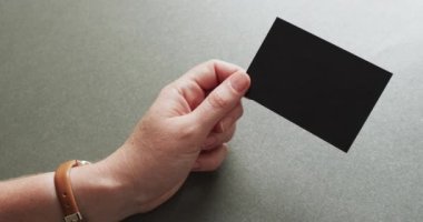 Beyaz bir kadının elinde gri arka planda siyah bir kartvizit var. Kopya alanı, ağır çekim. İş, iletişim detayları, modelleme, tasarım şablonu.