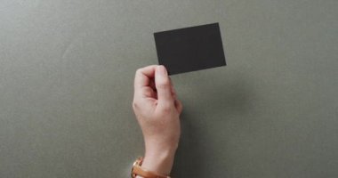 Beyaz bir kadının elinde gri arka planda siyah bir kartvizit var. Kopya alanı, ağır çekim. İş, iletişim detayları, modelleme, tasarım şablonu.
