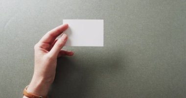 Beyaz kadın elinde gri arka planda beyaz kartvizit tutuyor. Kopya alanı, ağır çekim. İş, iletişim detayları, modelleme, tasarım şablonu.