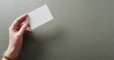 Beyaz kadın elinde gri arka planda beyaz kartvizit tutuyor. Kopya alanı, ağır çekim. İş, iletişim detayları, modelleme, tasarım şablonu.