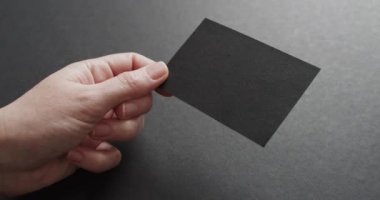 Beyaz bir kadının elinde gri arka planda siyah bir kartvizit var. Kopya alanı, ağır çekim. İş, iletişim detayları, modelleme, tasarım şablonu.