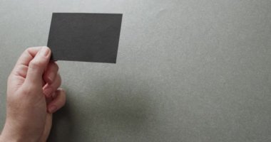 Beyaz bir kadının elinde gri arka planda siyah bir kartvizit var. Kopya alanı, ağır çekim. İş, iletişim detayları, modelleme, tasarım şablonu.