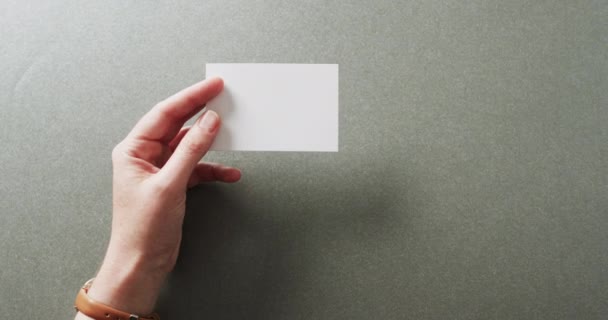 灰色の背景に白い名刺を持っている白人女性の手 コピースペース スローモーション ビジネス 連絡先の詳細 モックアップ デザインのテンプレート — ストック動画