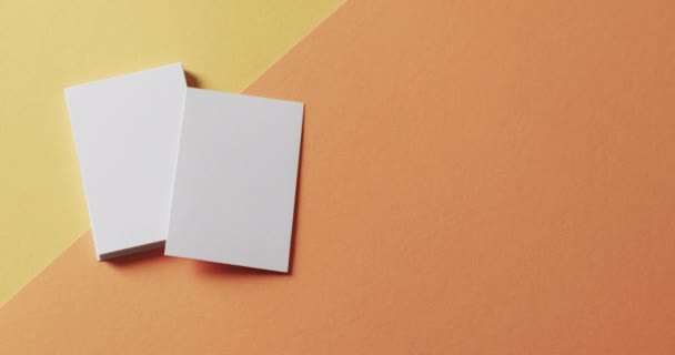 黄色とオレンジの背景に空白の白い名刺のオーバーヘッドビュー コピースペース スローモーション ビジネス 連絡先の詳細 モックアップ デザインのテンプレート — ストック動画