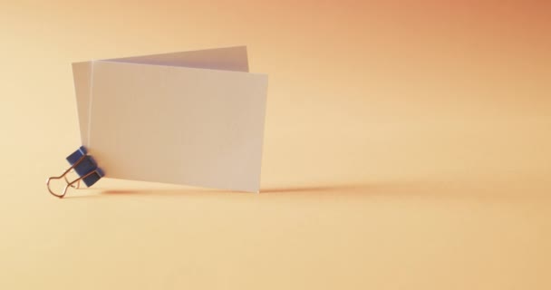 オレンジ色の背景にブルドッグクリップ付きの2つの空白のホワイトビジネスカード コピースペース スローモーション ビジネス 連絡先の詳細 モックアップ デザインのテンプレート — ストック動画