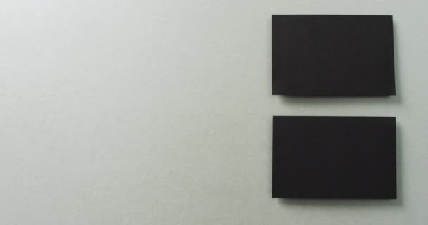 グレーの背景 コピースペース スローモーションに配置された2つのブラックビジネスカードのオーバーヘッドビュー ビジネス 連絡先の詳細 モックアップ デザインのテンプレート — ストック動画