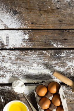 Yüksek açılı un manzarası yumurta karton, merdane, kaşık ve sarısı dağınık ahşap masada. değiştirilmemiş, yiyecek, kurabiye, malzemeler ve hazırlık konsepti.