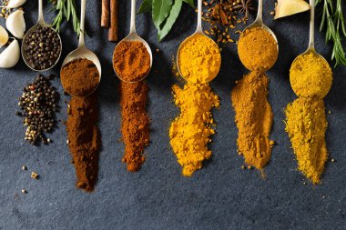 Siyah mermer masaya dizilmiş şifalı otlarla birlikte kaşıklardaki çeşitli baharatların tam üstünde. değiştirilmemiş, yiyecek, malzeme ve baharat konsepti.
