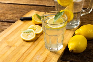 Limonata ve limonlu bardaklar ve masanın üstündeki kesme tahtasındaki yapraklarla yakın plan. Değiştirilmemiş, ahşap, içecek, sarı, turunçgil, yiyecek, sağlıklı konsept.