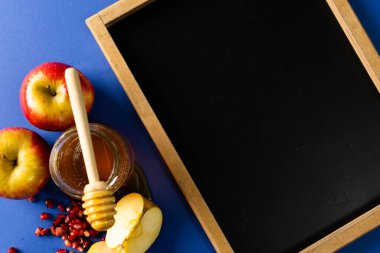 Mavi arka planda bal, elma ve nar içeren bir yazı tahtası. kopya alanı, eğitim, öğrenme, tatlı yiyecek, meyve, yiyecek, sağlıklı ve sonbahar mevsimi kavramı.