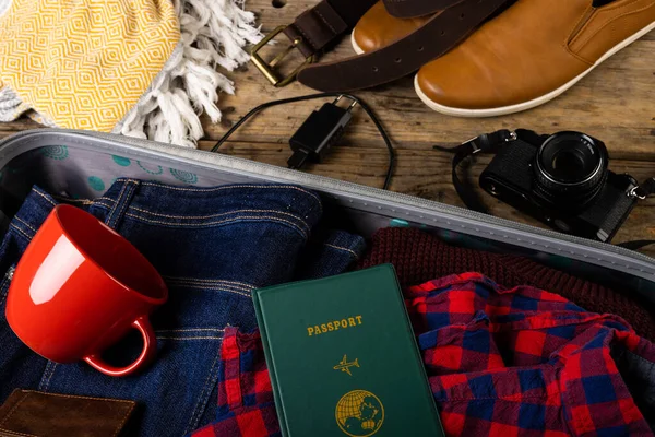 High angle view of clothes, passport and cup in suitcase by shoes, camera, belt and blanket on table. Accessories, unaltered, travel, luggage, fashion, vacation concept.