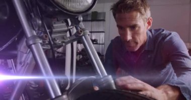 Garajda motorsiklet tamir eden beyaz erkek tamircinin üzerinde parlayan ışıkların animasyonu. Bisiklet haftası konsepti dijital olarak oluşturulmuş video.