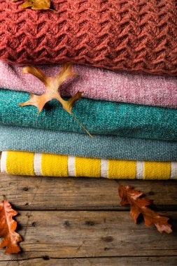 Ahşap masa üzerinde yapraklarla dolu renkli kazakların yüksek açılı görüntüsü. Değiştirilmemiş doğa, sıcak kıyafetler, akçaağaç yaprağı, sonbahar mevsimi konsepti..