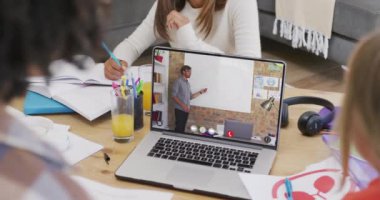 Çeşitli öğrenciler ekranda beyaz erkek öğretmenle çevrimiçi ders için dizüstü bilgisayar kullanıyor. İletişim, teknoloji, okul, öğrenme ve çevrimiçi eğitim, dijital kompozit video.