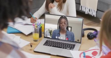 Farklı öğrenciler ekranda Afro-Amerikan kız öğrencilerle görüntülü görüşme için dizüstü bilgisayar kullanıyorlar. İletişim, teknoloji, okul, öğrenme ve çevrimiçi eğitim, dijital kompozit video.