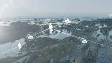 Bulutlu gökyüzüne karşı deniz kıyısındaki kayaların üzerindeki bağlı ikonların animasyonu. Dijital bileşik, çoklu pozlama, iletişim, okyanus, su, soyut ve teknoloji kavramı.