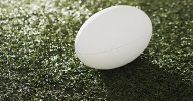Beyaz rugby topu güneş ışığıyla aydınlatılmış çimlerin üzerinde fotokopi alanı ile, yavaş çekim. Rugby, spor, yarışma ve oyunlar dijital olarak oluşturuldu.